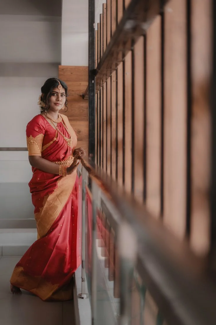 A woman in a red sari beside an ornate corridor