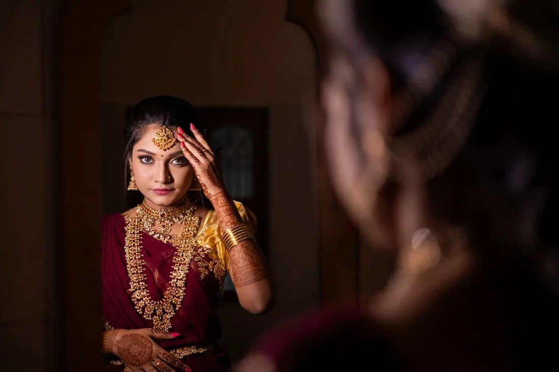 A bride in maroon, seen with her reflection in a mirror